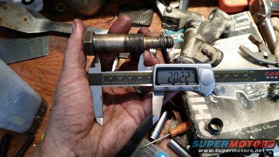 Measuring a bolt with digital calipers, reading 20.22mm. A Ford Bronco manual is visible in the background
