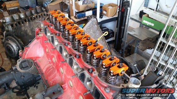 Engine block with orange rocker arms and valve springs. Some parts are on shelves in the background