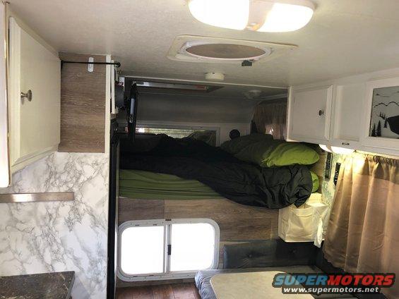 Camper interior with bunk beds, sleeping bags, cabinets, and a window