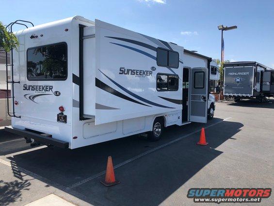 RV with slide-out extended, showing 'Sunseeker LE' badging on the rear. Another RV labeled 'Highlander' is parked behind it