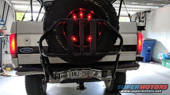 Rear view of a 1995 Ford Bronco with a spare tire mounted on a swing-away carrier. The brake lights are illuminated