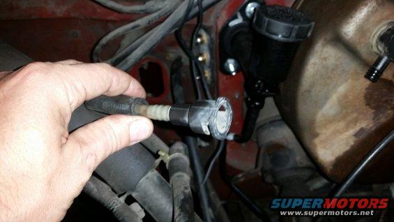 Hand holding a disconnected brake line near the master cylinder reservoir
