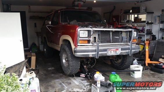 red 1985 Ford Bronco in garage, front end visible, hood is off, being worked on