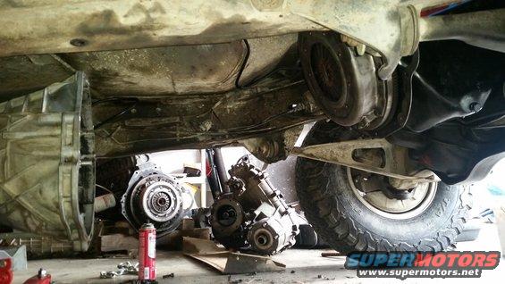 Underside of a vehicle showing transmission and transfer case removed for work. Parts are on the floor
