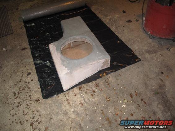 Gray custom subwoofer enclosure with a large circular cutout, placed on a black tarp on a concrete floor