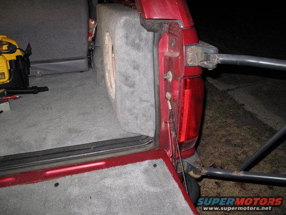 Red SUV interior with custom subwoofer box and gray carpet. Tailgate is open, showing a yellow power tool