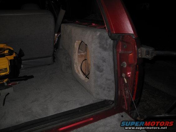 Red SUV interior with custom subwoofer box and yellow power tool. Rear door open