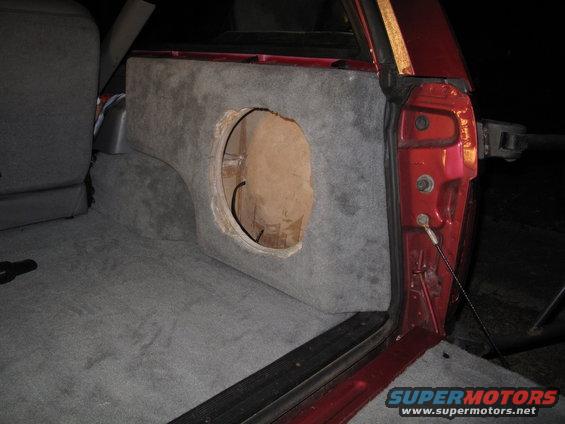 custom carpeted subwoofer box installed in the rear of a vehicle, with an open hole for a speaker