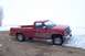 1988 Chevrolet Silverado 2500 - A red pickup truck sits on a dirt patch with snowdrifts to its right and a bare tree in the distance.