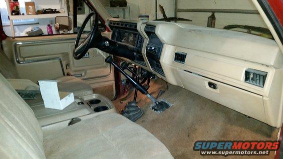 Interior of a tan 1980s Ford truck or SUV, showing dashboard, steering wheel, and center console with dual shifters