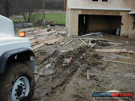 Construction site with muddy tire tracks and lumber scattered near a building under construction