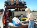1996 Ford Bronco - A family prepares for a trip, loading a red SUV with gear and children while enjoying snacks.