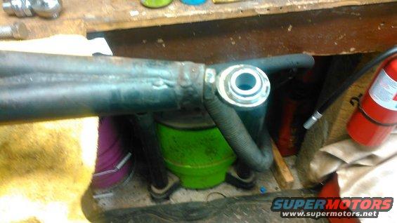 Close-up of a metal bar with a bushing and a flexible hose attached, resting on a workbench