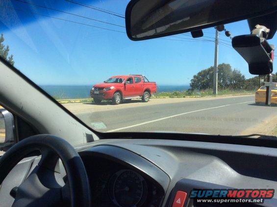 Red pickup truck parked by the ocean, seen from inside a car