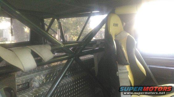 Roll cage and yellow racing seat inside a vehicle, with a diamond plate toolbox visible