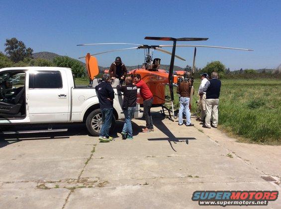 White pickup truck parked next to an orange helicopter with people around it