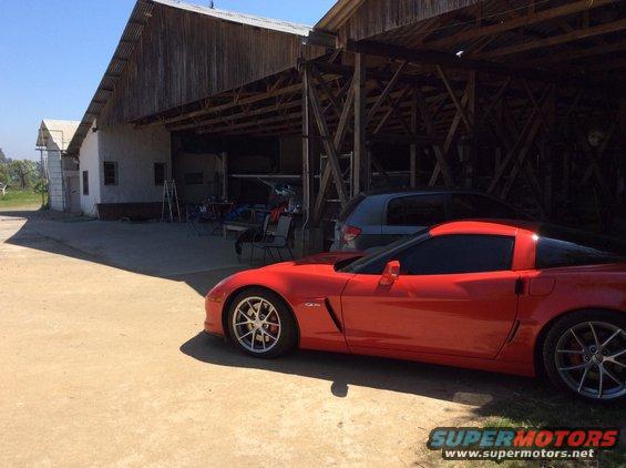 Red sports car parked in front of a barn, with a grey SUV behind it