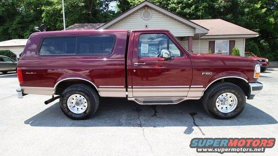Maroon Ford F-150 pickup with a tan stripe and a camper shell, seen from the side