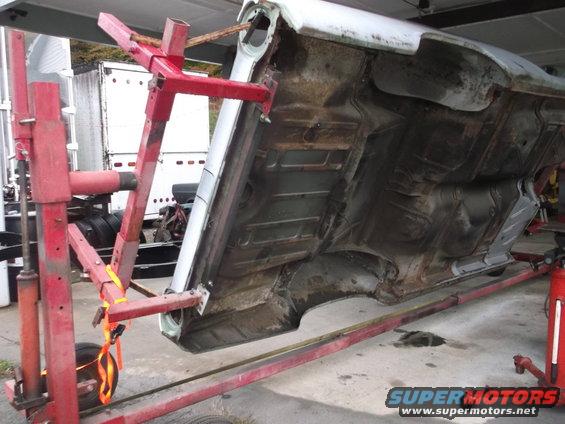 Undercarriage of a car supported by red jack stands, showing suspension and frame components