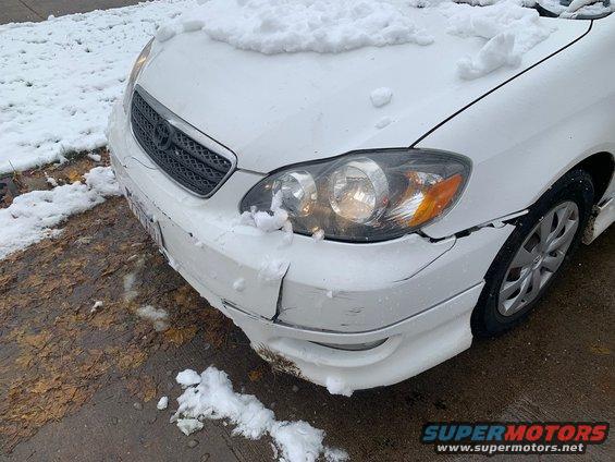Front of a white sedan with snow on the hood and a cracked front bumper