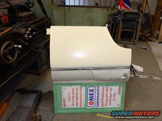 Cream-colored car door with chrome trim and handle, resting on green boxes with lubricant advertisements
