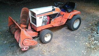 Orange and white Simplicity snowblower attachment on a riding mower, parked on asphalt