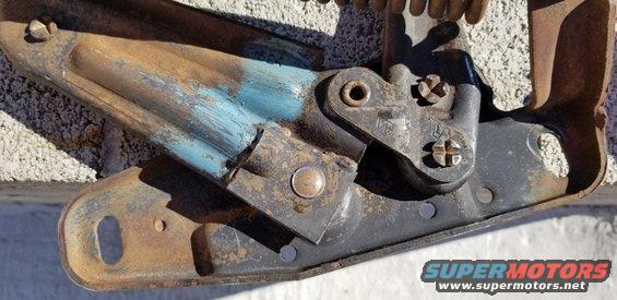 Rusty hood hinge mechanism with blue paint remnants and visible screws