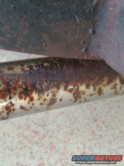 Close-up of a rusted metal pipe attached to a bracket, showing significant corrosion