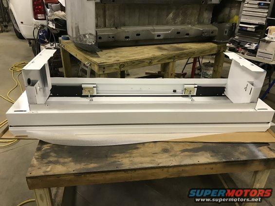 White vehicle part with black and metal components, resting on a wooden workbench