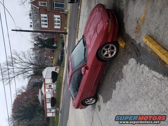 Red coupe parked on pavement, houses and trees in background
