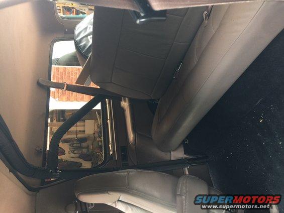 Interior shot of a vehicle, showing front and rear seats, seatbelts, and a roll bar