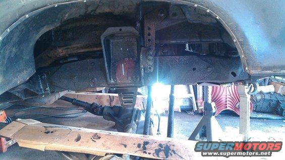 Vehicle frame and suspension parts on jack stands, with visible rust and modifications