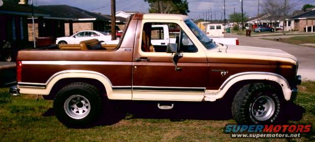 Brown and tan Ford Bronco parked on grass. It has a removable top and a step bar