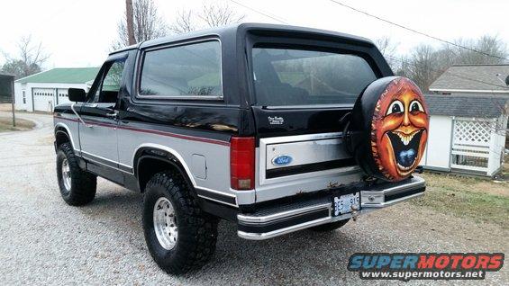 1986 Ford Bronco rear view, silver and black two-tone paint, custom painted spare tire cover with a face