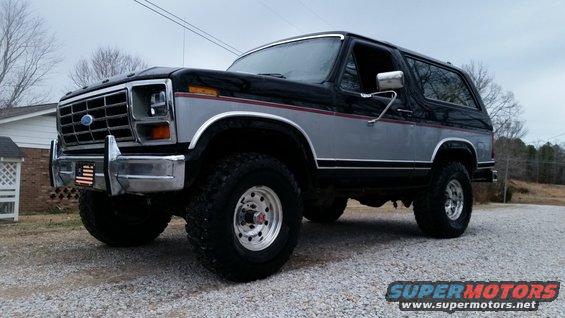 Black and silver Ford Bronco with aftermarket wheels parked on gravel