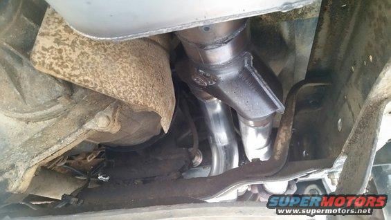 Close-up of a vehicle's exhaust manifold and pipes, showing new shiny metal and some rust