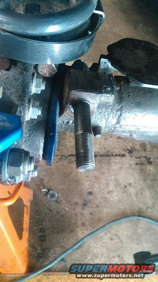 Front axle assembly with a threaded stud protruding from a metal housing, near a coil spring