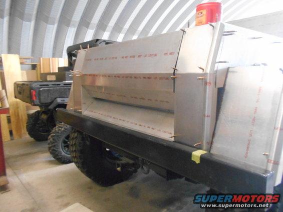Custom truck bed modification with visible text on panels. Another vehicle is parked behind