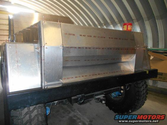 Aluminum body panels riveted together on a vehicle chassis, with large off-road tires visible