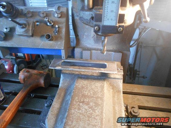 Milling machine cutting a slot in a metal plate held in a vise. Drill bit is lowered, and a ruler shows depth