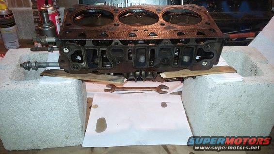 Engine cylinder head resting on concrete blocks with wrenches below