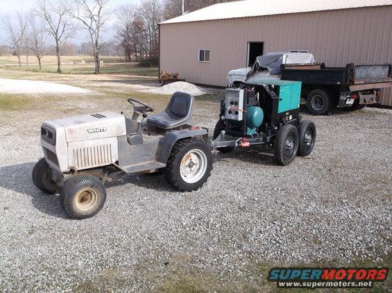 White riding mower towing a generator trailer. Dump truck in background