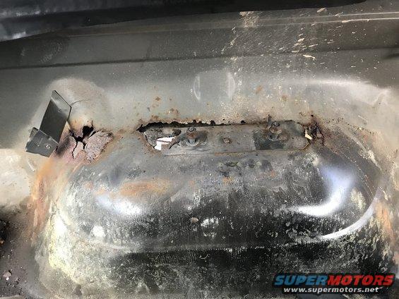 Rusted vehicle floor pan with a metal bracket and holes from corrosion