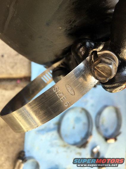 Metal hose clamp with 'SIZE 6' and Ford logo stamped on it, with other clamps blurred in background