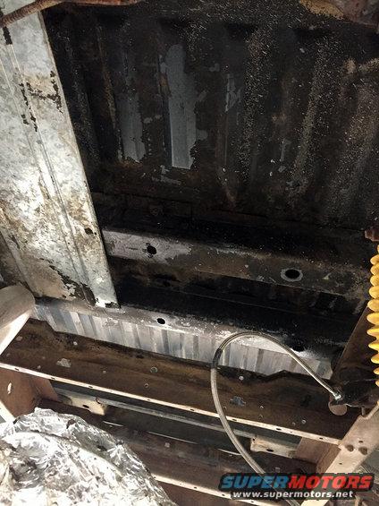 Undercarriage of a vehicle with rust and some exposed metal framing. A yellow shock absorber is visible on the right