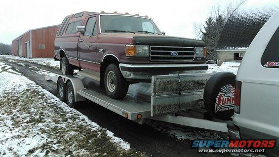 Maroon 1991 Ford F-150 with a camper shell on a trailer, being towed by another vehicle