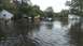 2006 Honda RANCHER - Submerged vehicles sit in floodwaters on a suburban street, with houses and trees visible in the background.