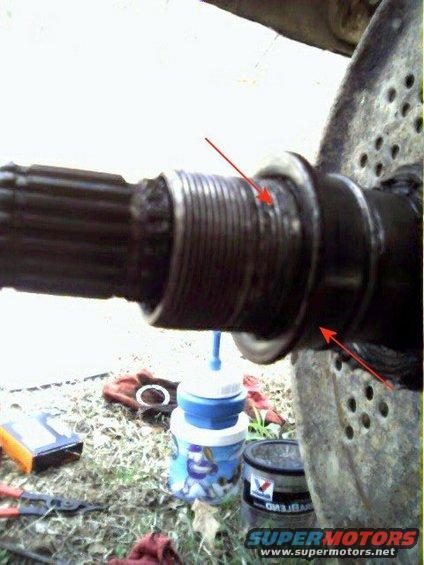 Splined axle shaft with red arrows pointing to wear marks on threads, next to a blue fluid dispenser and tools