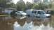 2006 Honda RANCHER - A white van and sedan are partially submerged in floodwaters, with houses and trees visible in the background.