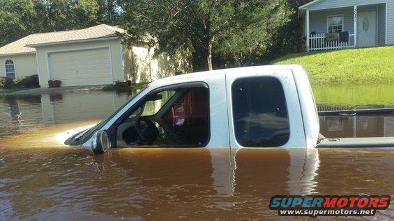 White pickup truck submerged in floodwater, showing interior and side profile